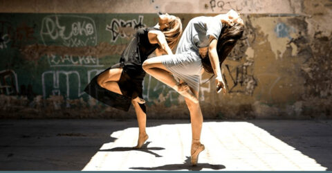 2 jeunes femmes dansent devant un mur taggué
