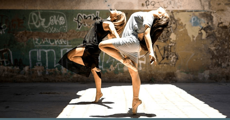 2 jeunes femmes dansent devant un mur taggué