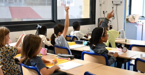 classe avec élèves qui lèvent la main pour répondre à la maitresse